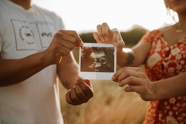 a couple holding an ultrasound picture against a natural backdrop