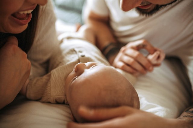 a man and woman laying on a bed with a baby smiling